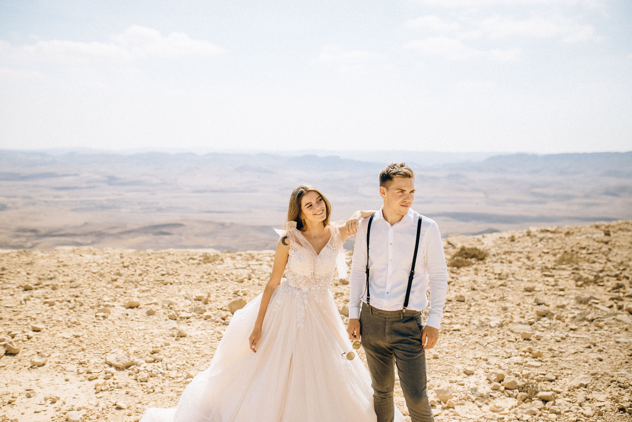 A couple in wedding attire enjoying a romantic moment in a stunning desert landscape.