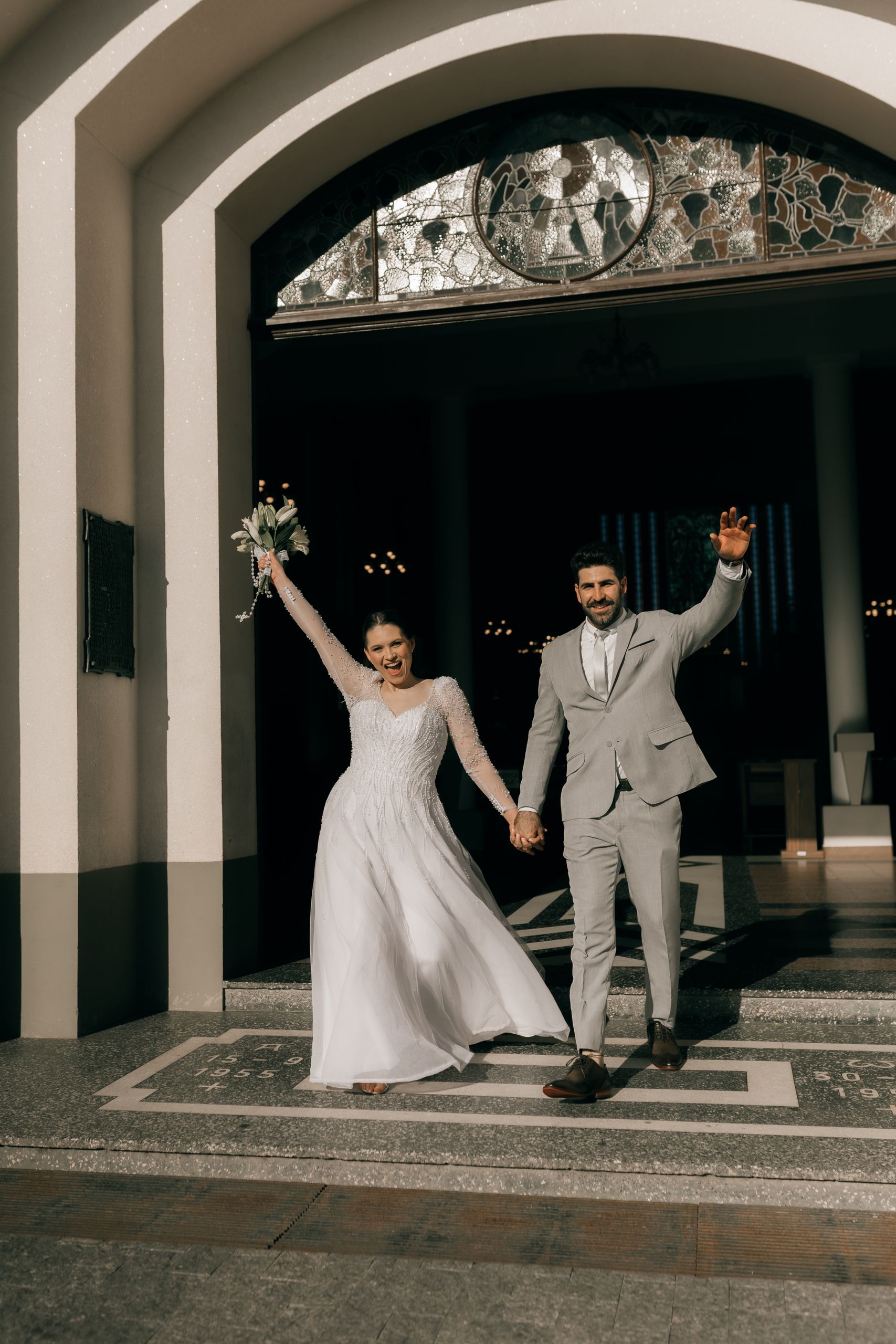 A joyful couple exits the church, celebrating their wedding day in sunlight.